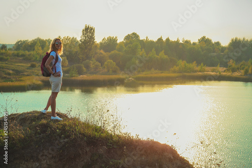 Young woman with pink backpack is standing on the blue chalk quarries background close up in sunset time