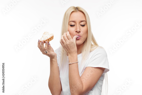 Diet. Dieting concept. Image of beautiful blond woman in white clothe isolated over white background holding and eating cake with pleasure 