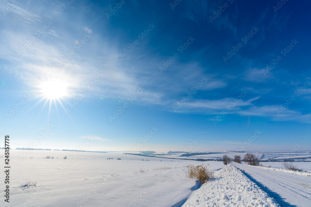 winter landscape. white snowy road, blue sky, trees covered with frost