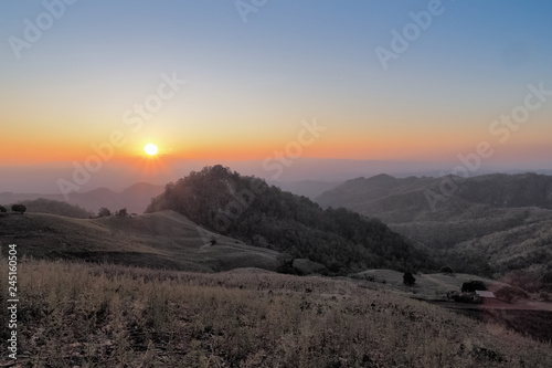 sunset at Doi Samur Dao, mountain view evening of green hill and forest cover with soft mist with yellow sun light in the sky background, Sri Nan National Park, Nan province, Thailand.