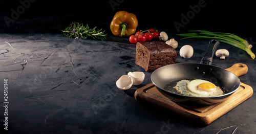 Fried egg on a frying pan surrounded by vegetarian cuisine ingredients on dark table