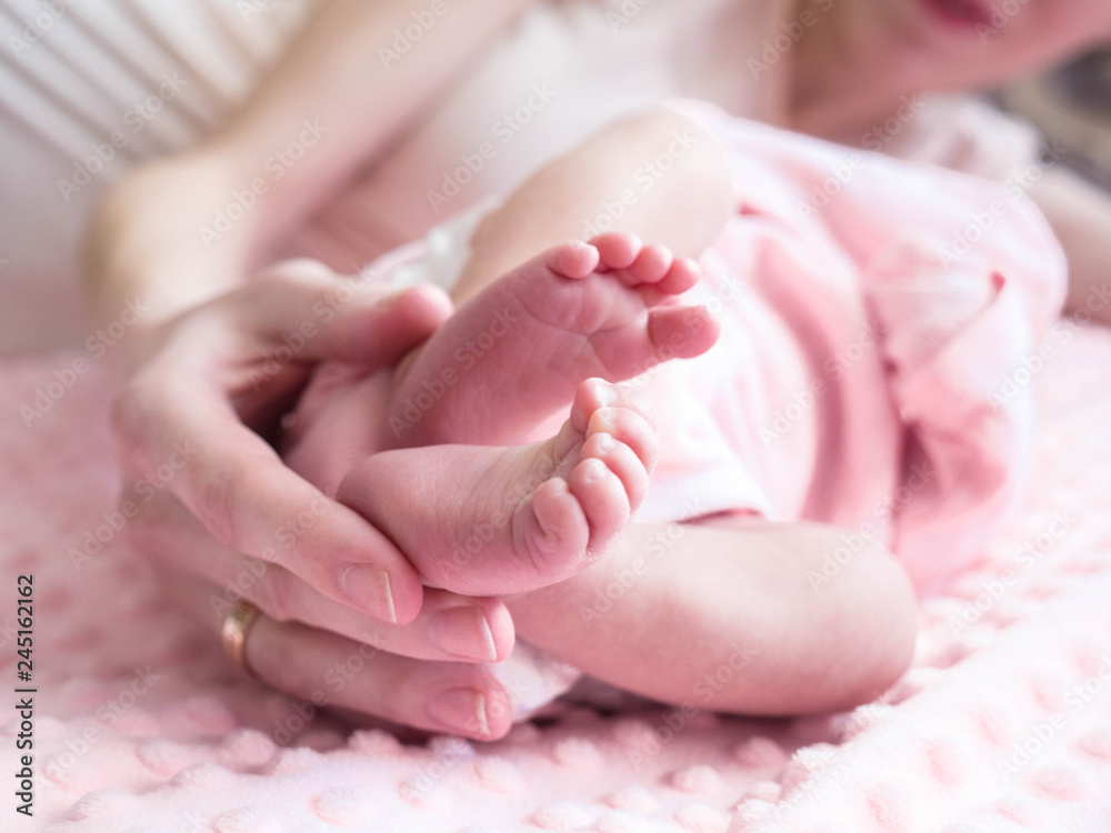 Mother holds tiny feet of her baby-girl lying on pink blanket. Cute baby legs in the parents hands. Baby's foot in mother hands. Mother holds tiny feet of her baby-girl lying on pink blanket. Cute baby legs in the parents hands. Baby's foot in mother hands.
