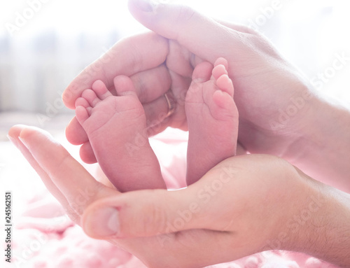 Father holds tiny feet of her baby-girl lying on pink blanket. Cute baby legs in the parents hands. Baby's foot in father hands.