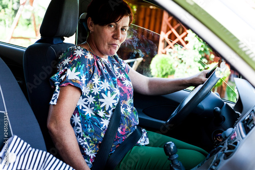 Middle aged woman sitting insie the modern car. The lady driver smiling behind the wheel looking cheerful. Doing weekly shop for household commodities. City lifestyle concept. photo