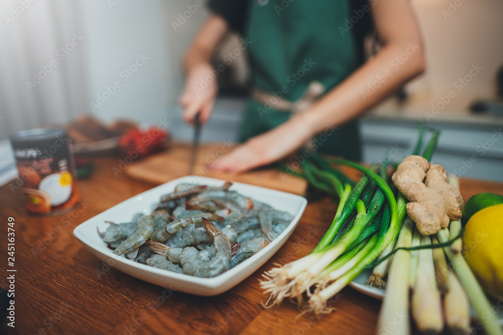 Closeup image of young female cooking in the modern kitchen, focus on fresh tiger prawns and green onion, ingredients for thai soup tom yum, food blogger concept