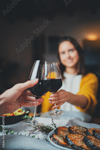 Vertical image of romantic couple making cheers with glasses of red wine, young sweet couple dining at night in cozy restaurant with healthy food, Celebration Cheers Dinner Love Concept