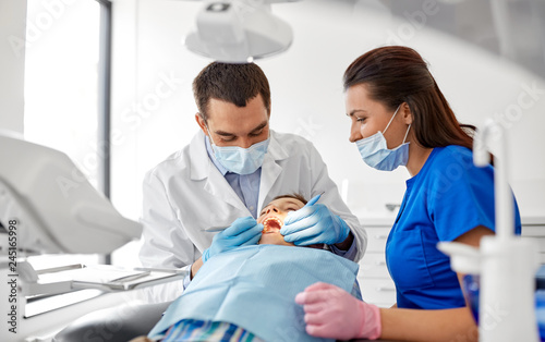 medicine, dentistry and healthcare concept - dentist with mouth mirror and probe checking for kid patient teeth at dental clinic
