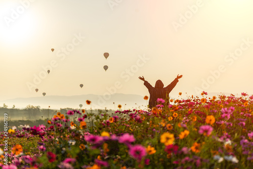 Lifestyle traveler women raise hand feeling good relax and happy freedom and see the fire balloon outdoors the nature tea and cosmos farm in the sunrise morning. Travel and summer Concept photo