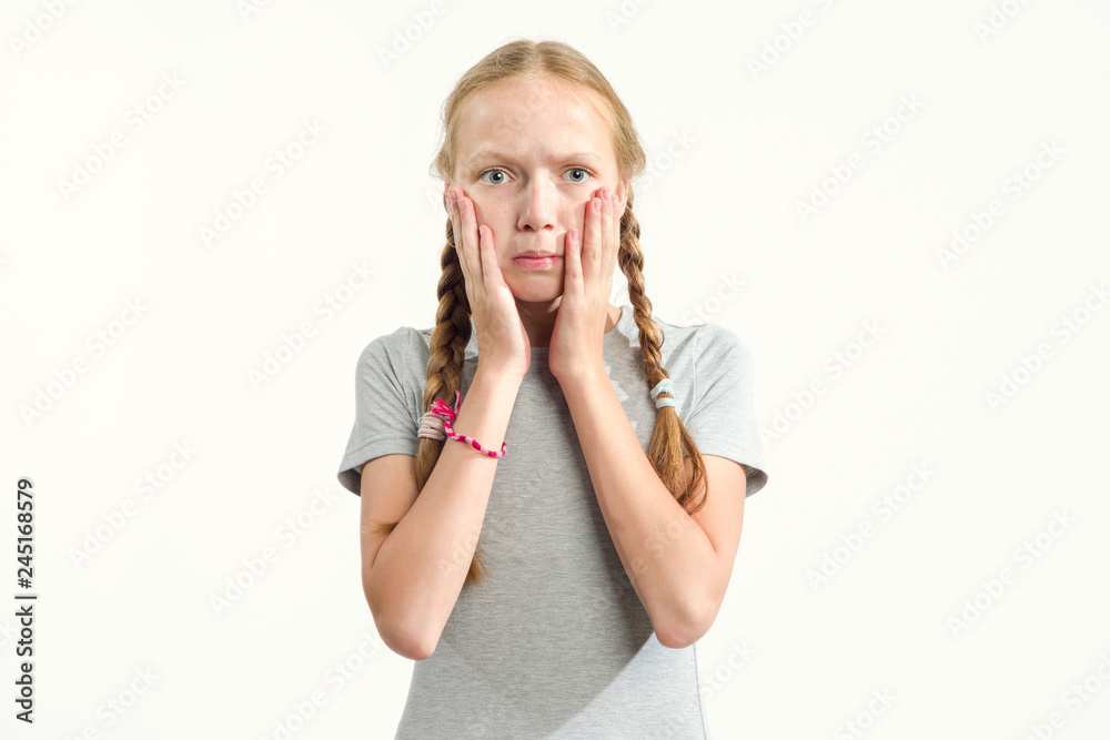 Fototapeta premium Surprised girl holds hands on face. 13 years old girl on a light background. Emotion of surprise.