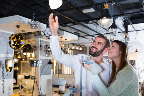 Smiling couple customers choosing floor lamp in store