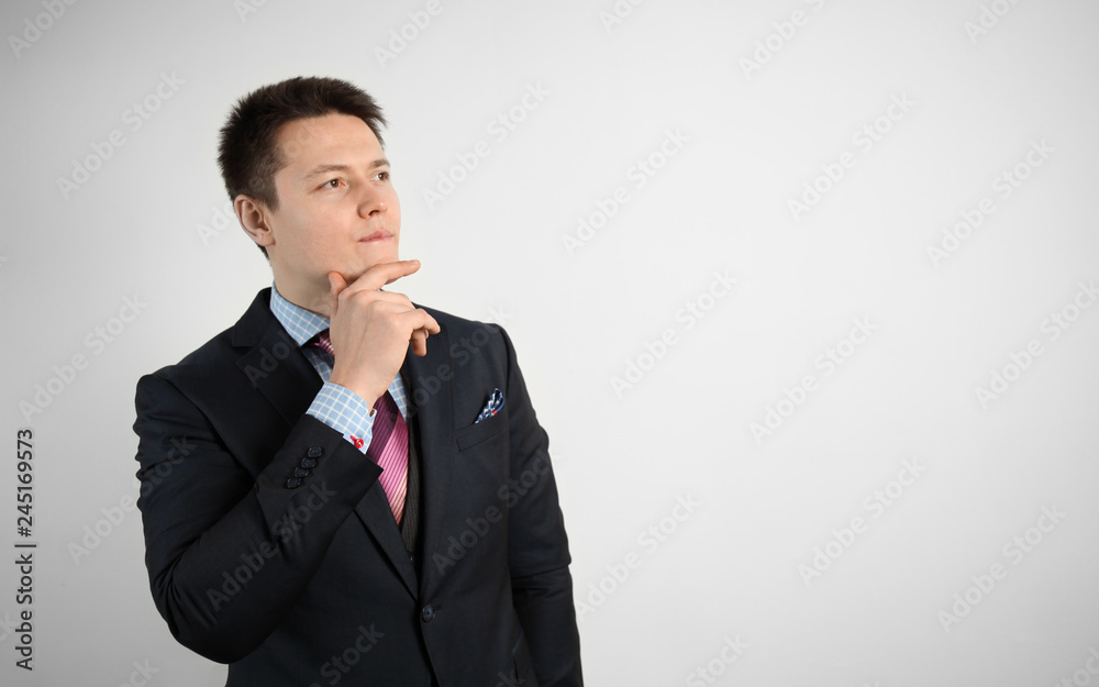 Young businessman in suit on gray background is thinking over question or problem. Young businessman in suit on gray background is thinking over question or problem.