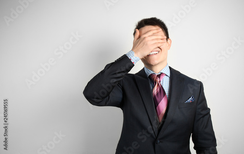 Young businessman in suit on gray background face palm and smiling.