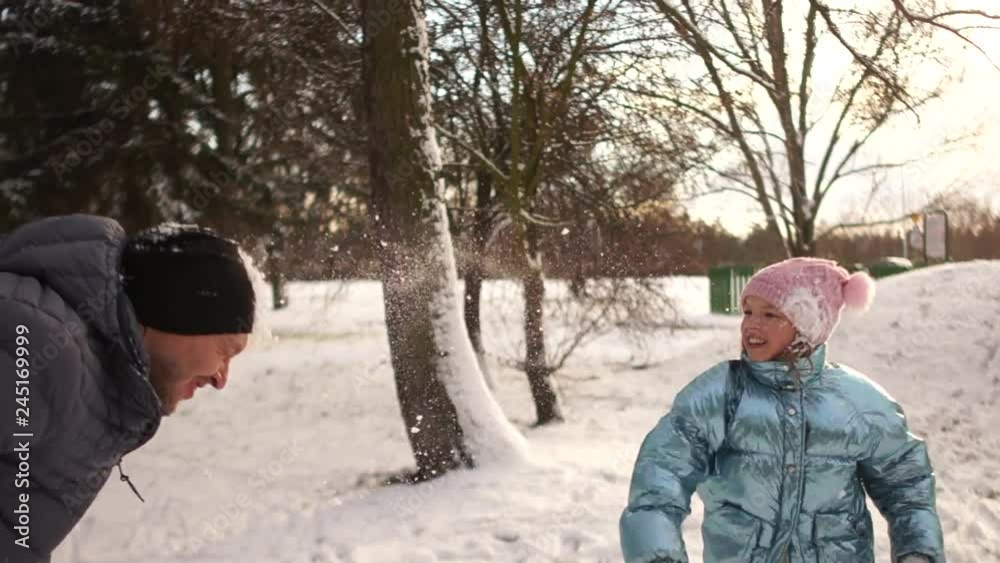Cheerful snow fight. Father and daughter fall into each other with snowballs. Happy family holidays, winter weekends, a walk in the winter park Cheerful snow fight. Father and daughter fall into each other with snowballs. Happy family holidays, winter weekends, a walk in the winter park