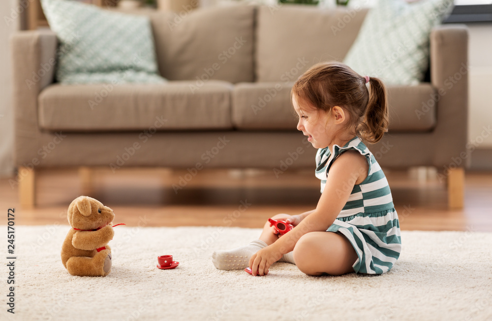 childhood and people concept - happy three years old baby girl playing tea party with toy crockery and teddy bear at home