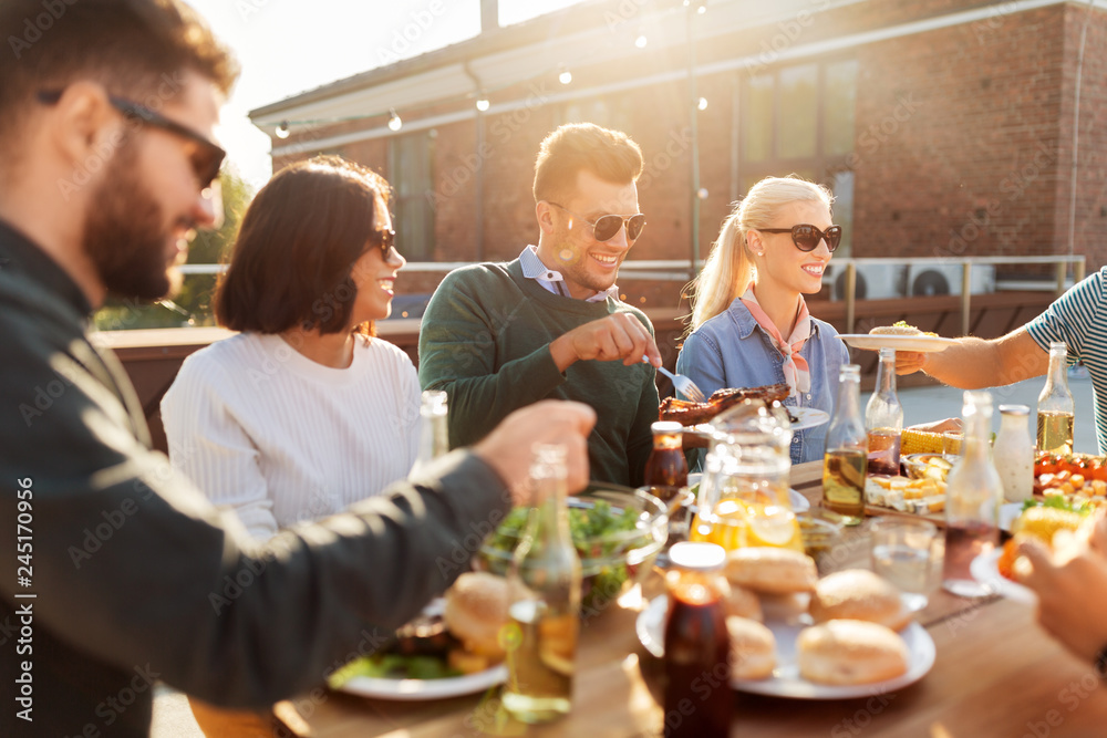 leisure and people concept - happy friends eating and drinking at barbecue party on rooftop in summer