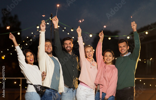 leisure, celebration and people concept - happy friends with sparklers at rooftop party at night