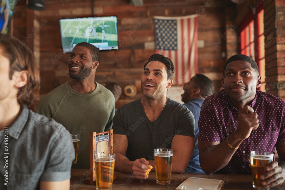 Male Friends Drinking Beer And Watching Game On Screen In Sports Bar Male Friends Drinking Beer And Watching Game On Screen In Sports Bar