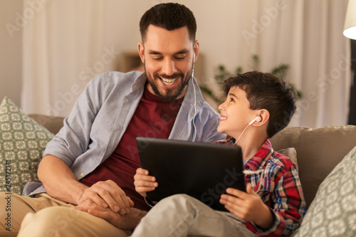family  fatherhood and technology concept - happy father and little son with tablet pc computer and earphones listening to music at home