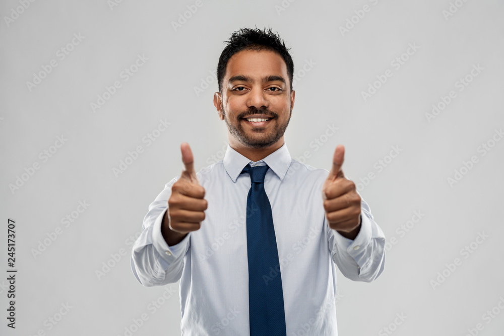 business, office worker and people concept - smiling indian businessman in shirt with tie showing thumbs up over grey background business, office worker and people concept - smiling indian businessman in shirt with tie showing thumbs up over grey background