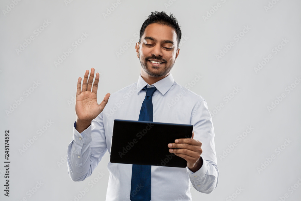 business, office worker and people concept - smiling indian businessman having video call on tablet pc computer over grey background business, office worker and people concept - smiling indian businessman having video call on tablet pc computer over grey background