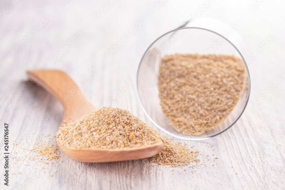 Oat bran in a wooden spoon and in a glass transparent glass on a white wooden table Oat bran in a wooden spoon and in a glass transparent glass on a white wooden table