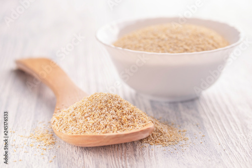 Dry oat bran in a white plate on a light wooden table with a wooden spoon.