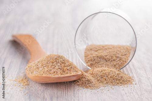 Oat bran in a wooden spoon and in a glass transparent glass on a white wooden table