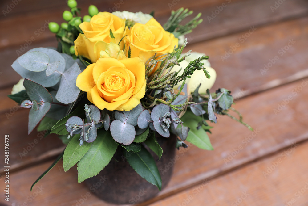 Festive flower arrangement of yellow roses, eucalyptus leaves and other plants on wooden background.