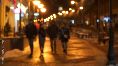 unfocused people are wolking on the road. people are dressed in warm winter clothes. a leisurely stroll after sunset. a lot of street lamps. winter photo