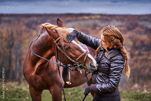 a young woman with brown hair gently communicates with her beloved horse. Autumn cloudy day.