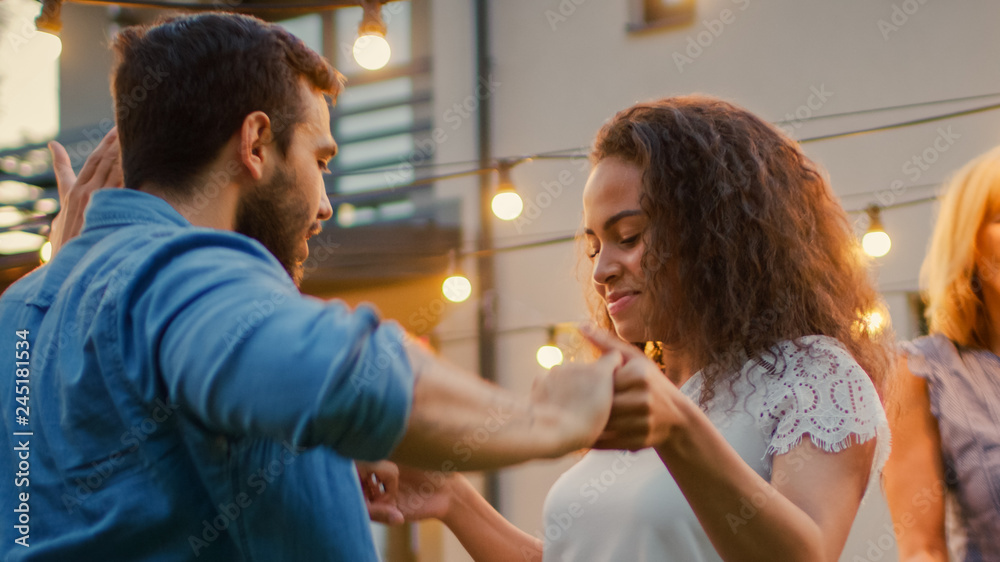 Romantic Couple Dances Together with Group of Friends at the Garden Party Celebration. Beautiful and Handsome People Having Fun one at the House Backyard on one Summer Evening. Romantic Couple Dances Together with Group of Friends at the Garden Party Celebration. Beautiful and Handsome People Having Fun one at the House Backyard on one Summer Evening.