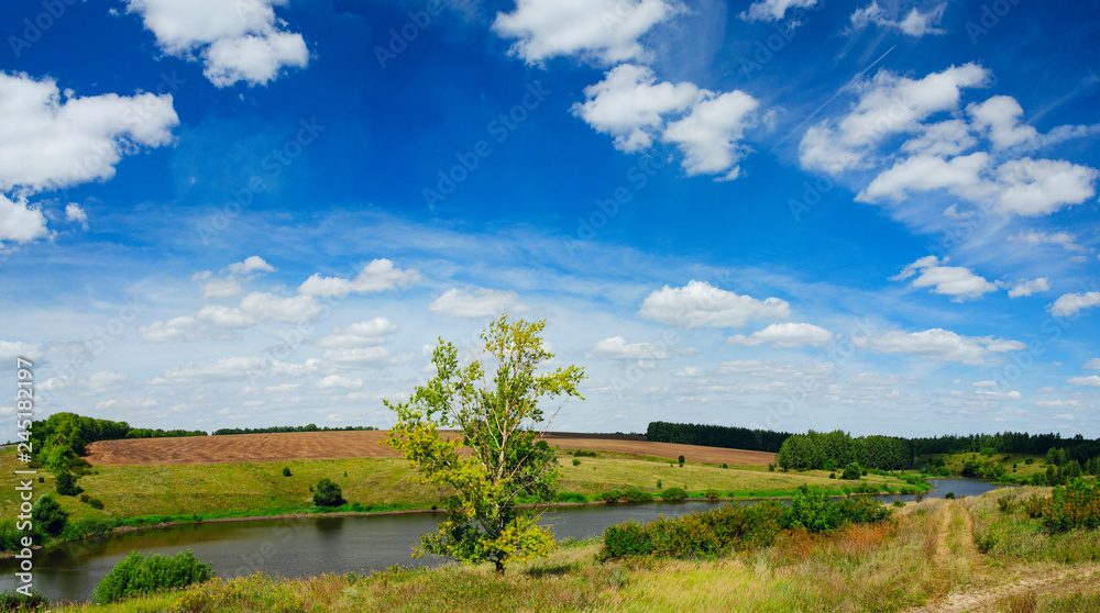 Sunny summer panoramic landscape with green hills,river,fields and distant woods.Beautiful fluffy clouds in blue sky on a nice day.