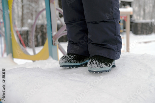 Child on the playground, legs in felt boots close-up against the background of snow, winter season.