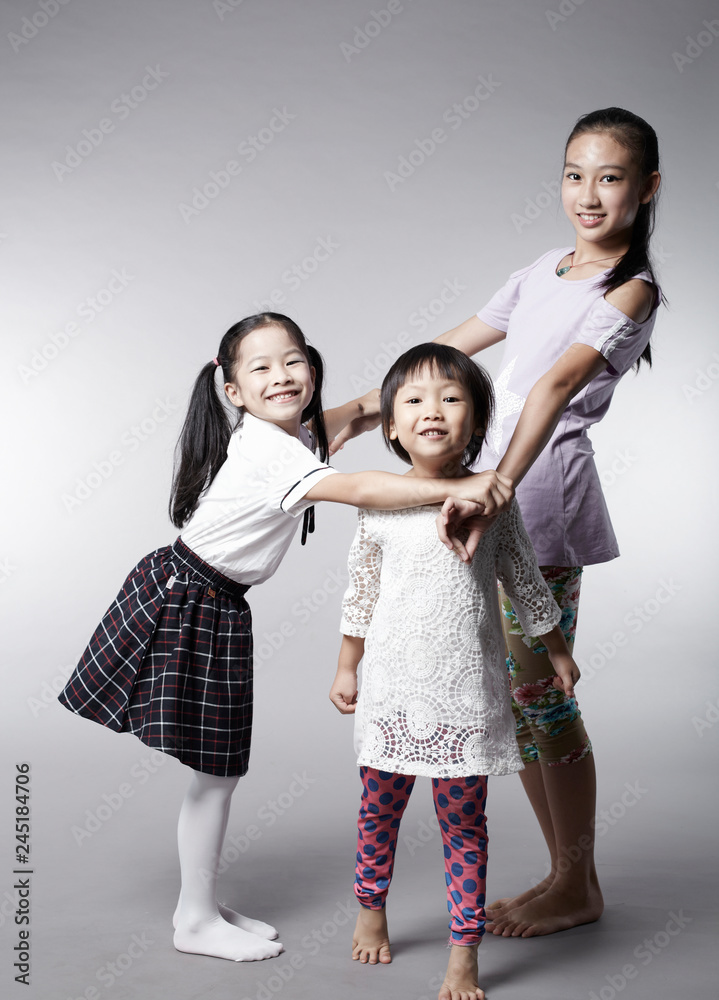 Three cute Asian Chinese little girls interacting happily, indoors with white background