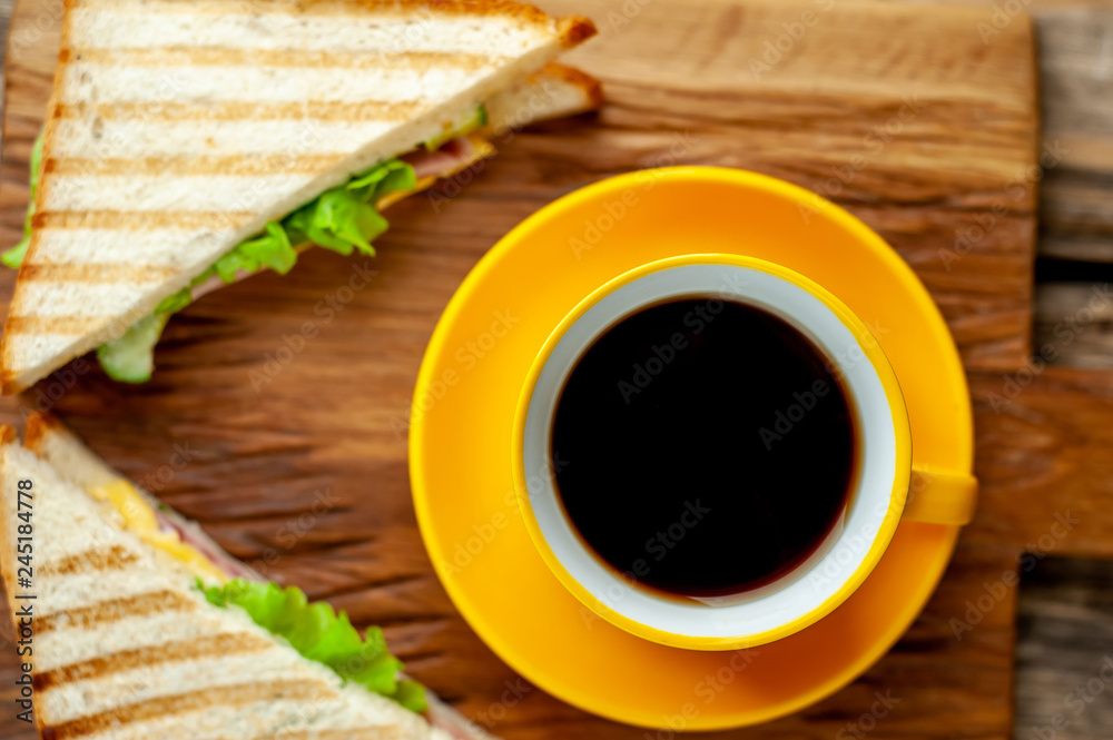 two delicious sandwiches with ham, cheese, lettuce and a cup of coffee on a wooden background two delicious sandwiches with ham, cheese, lettuce and a cup of coffee on a wooden background