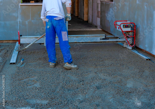 Worker on a laser screed machine leveling fresh poured concrete surface on a construction site