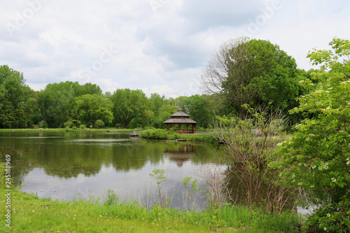 Midwest nature background with city park view. Beautiful late spring cloudscape with trees around the pond and wooden gazebo in a city park. Lakeview park, Middleton, Madison area, WI, USA.