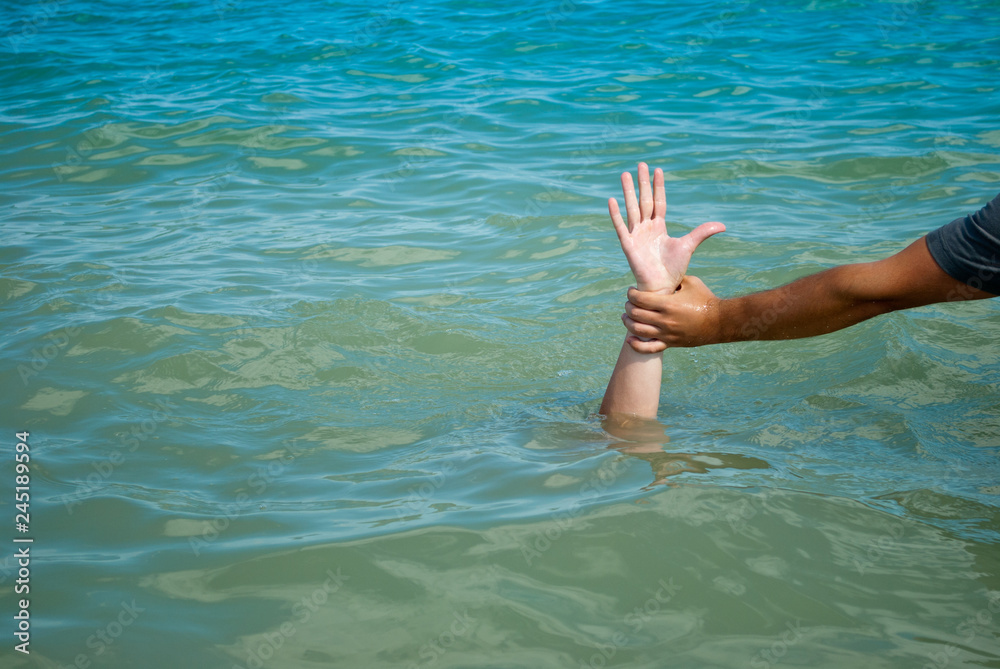 A man's hand drowns in water calling for help, man helps rescue, against the background of the sea and sky clouds summer, sun, weekend, can not swim, rescue, vacation wave foam
