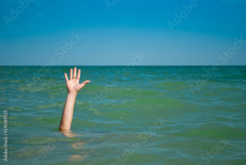 A man's hand drowns in water calling for help, against the background of the sea   and sky clouds summer, sun, weekend, can not swim, rescue, vacation wave foam