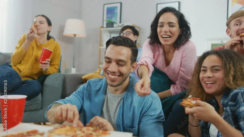 At Home Diverse Group Friends Watching TV Together, They Share Gigantic Pizza, Eating Tasty Pie Pieces. Guys and Girls Watching Comedy Sitcom or a Movie, Laughing and Having Fun Together. At Home Diverse Group Friends Watching TV Together, They Share Gigantic Pizza, Eating Tasty Pie Pieces. Guys and Girls Watching Comedy Sitcom or a Movie, Laughing and Having Fun Together.