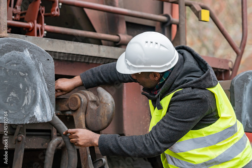 African American mechanic wearing safety equipment (helmet and jacket) checking gear train