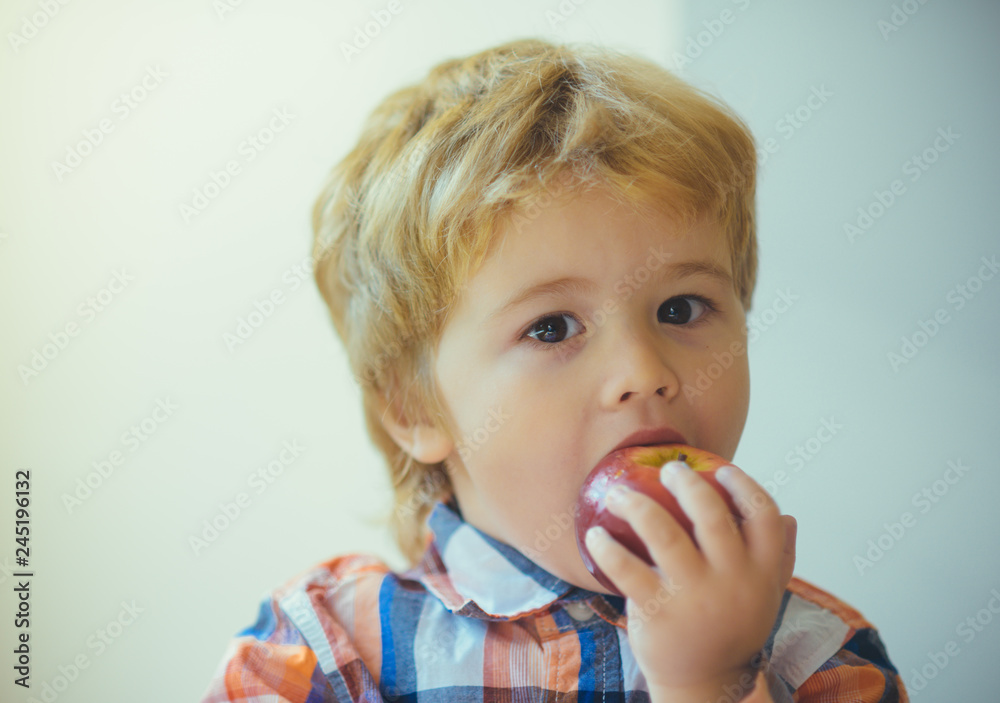 Cute toddler child eating red apple in hands on the day of valentine. Little blond boy with red delicious apple on white background. Child portrait with food. Cute toddler child eating red apple in hands on the day of valentine. Little blond boy with red delicious apple on white background. Child portrait with food.
