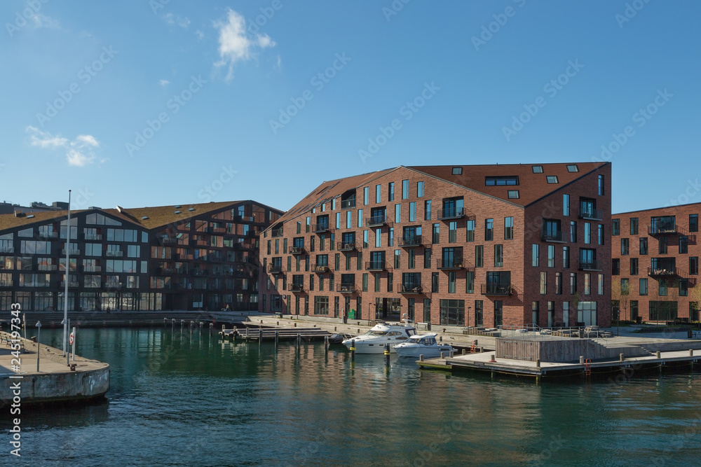 COPENHAGEN, DENMARK. Waterfront of Christianshavn district with boats and residential buildings, modern interpretation of the historic warehouses that characterize the area.