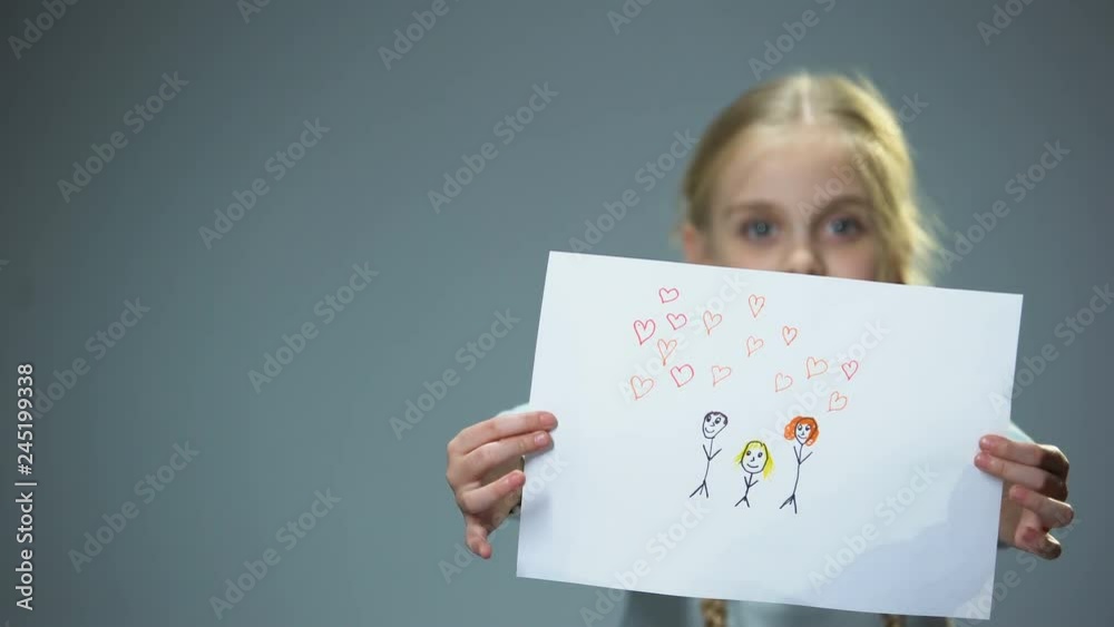 Happy little girl showing family picture into camera, feeling parental love Happy little girl showing family picture into camera, feeling parental love
