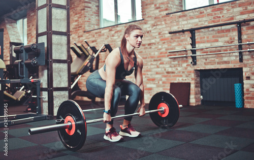 Fitness girl in sportswear doing deadlift exercise with barbell at gym.