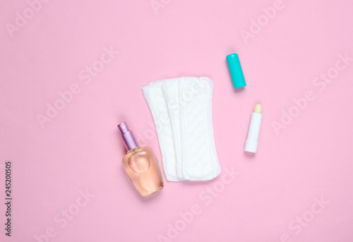 Women's beauty and hygiene products on a pink pastel background. Perfume bottle, hygienic lipstick, pads. Flat lay style.