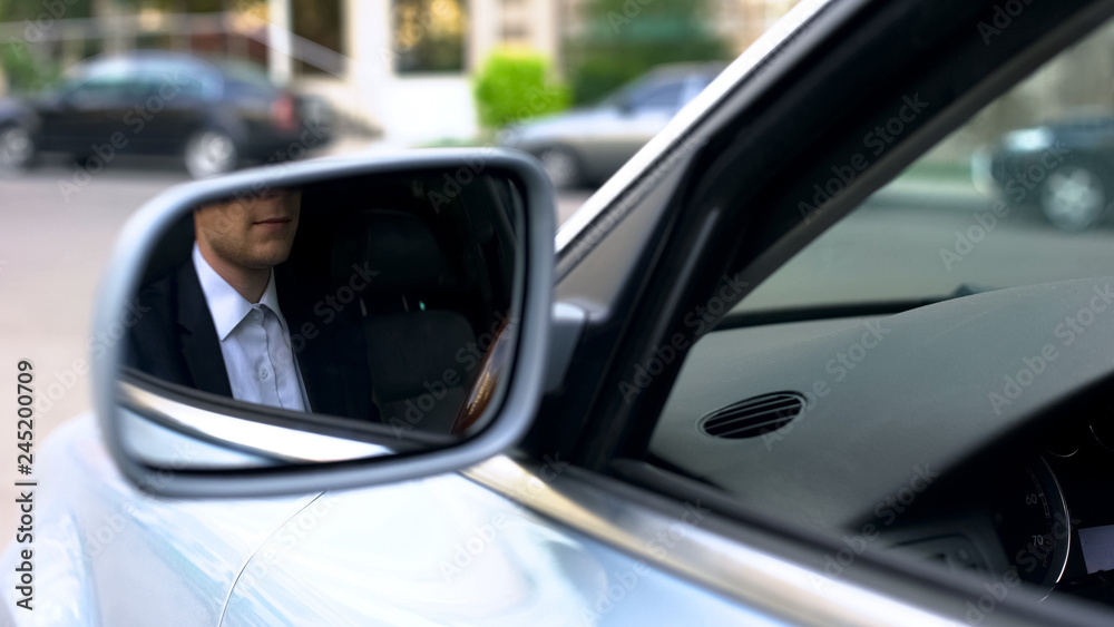 Young businessman reflecting in wing mirror of car, driving to office meeting