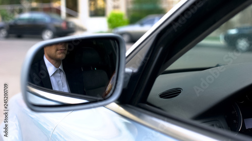 Young businessman reflecting in wing mirror of car, driving to office meeting © motortion