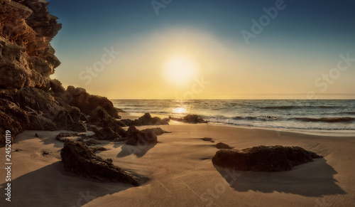 Beautiful sunset on the deserted Namibe beach. Photograph taken near the ground with cliff and rocks. Africa. Angola.