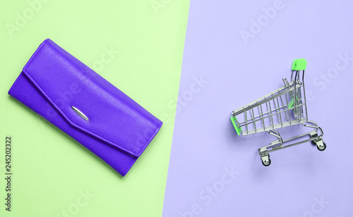 Violet purse and mini shopping trolley for purchases on a colored pastel background, consumer concept, minimalism, top view..